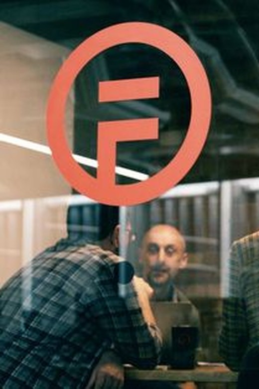The Flawless AI F logo on a glass office wall, with colleagues meeting behind it